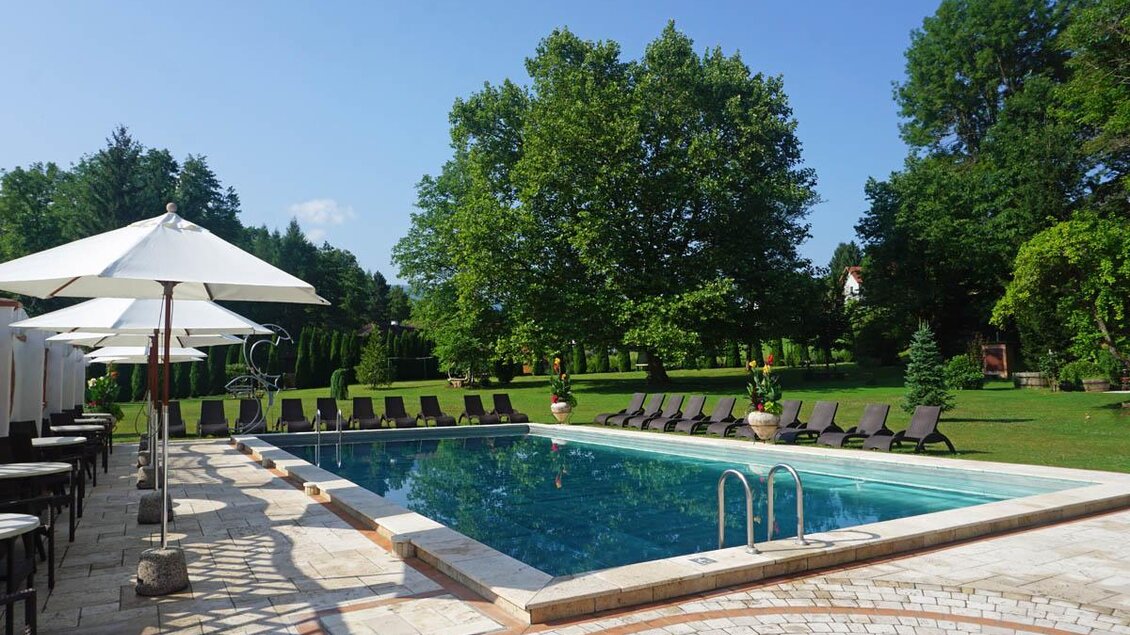 Ein schöner Außenpool umgeben von Liegen und Sonnenschirmen. Grüne Bäume und eine gepflegte Gartenlandschaft schaffen eine entspannte Atmosphäre. | © Desiree Zwanzleitner