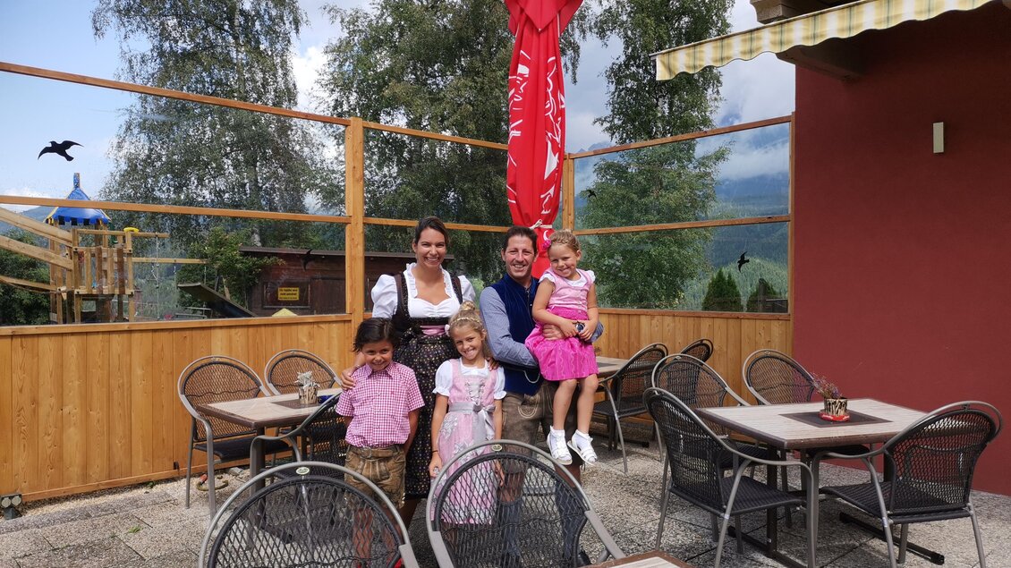 Familie steht auf einer Terrasse mit Tischen und Stühlen. Im Hintergrund sind Bäume und ein blauer Himmel sichtbar. | © Hotel Pariente