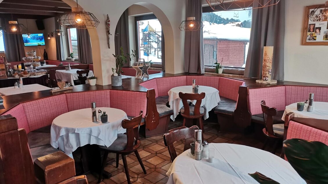 Ein gemütliches Restaurant mit runden und eckigen Tischen. Die Einrichtung ist rustikal, mit hellen Tischdecken und Holzstühlen, und es gibt große Fenster mit Blick nach draußen. | © Hotel Pariente