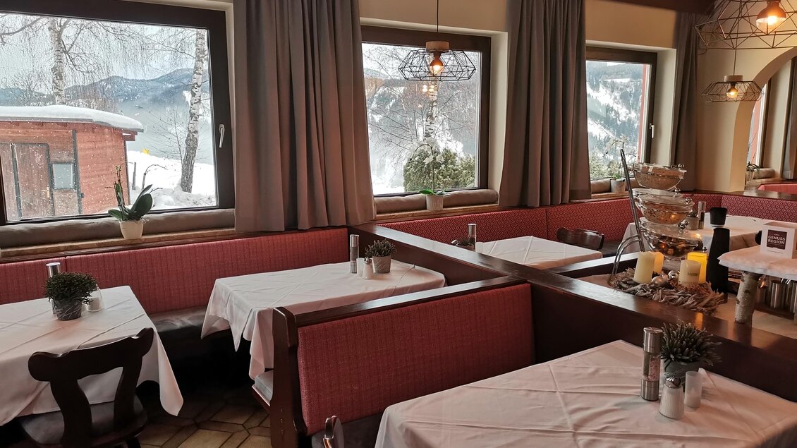 Ein gemütliches Restaurant mit Holzmöbeln und hübscher Fensteransicht. Draußen ist Schnee zu sehen und die Tische sind mit weißen Tischdecken gedeckt. | © Hotel Pariente