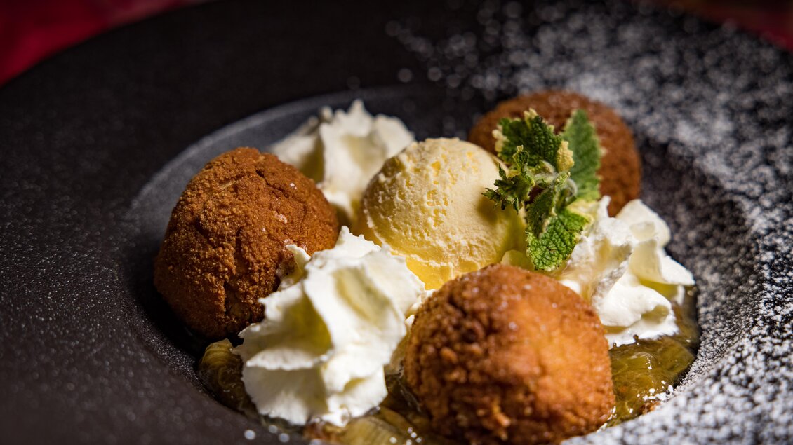 Ein köstliches Dessert auf einem schwarzen Teller. Es besteht aus frittierten Bällchen, einem Kugel Eis und Sahne, dekoriert mit frischer Minze. | © AMA