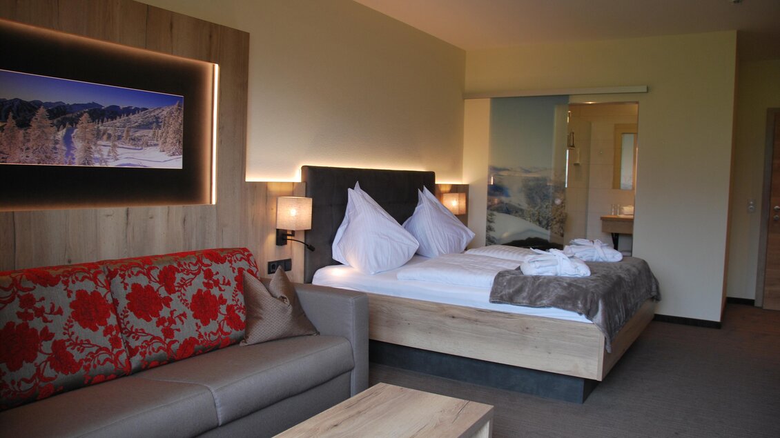 Ein modernes Hotelzimmer mit einem großen Bett und einem gemütlichen Sofa. Die Wände sind in warmen Tönen gehalten, und es gibt eine stilvolle Beleuchtung. | © Algo