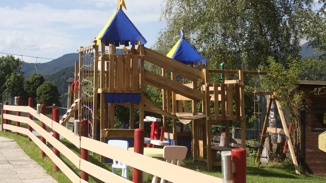 Ein schöner Spielplatz mit einer Holzspielanlage und bunten Zelten. Umgebung mit Grünflächen und einem Holzgeländer. | © Hotel Pariente