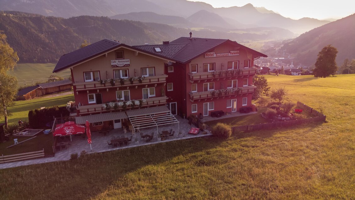 Ein malerisches Gebäude inmitten einer grünen Wiese mit Bergen im Hintergrund. Der Sonnenuntergang sorgt für eine warme, einladende Atmosphäre. | © Julius Kotus