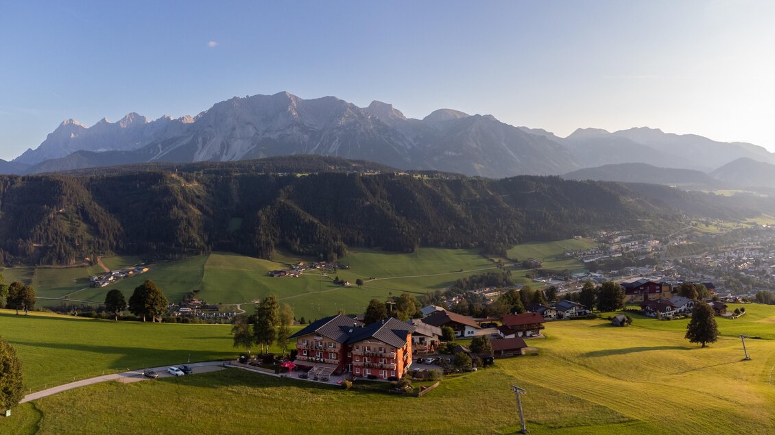 Eine malerische Landschaft mit hohen Bergen und grünen Wiesen. Im Vordergrund sind einige Gebäude und Bäume sichtbar. | © Julius Kotus