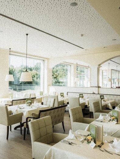 An elegant restaurant with bright interiors and large windows. The tables are beautifully set and offer a view of nature. | © Heilthermen Resort BW