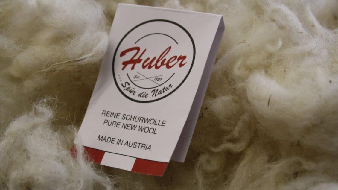 Ein Etikett mit der Aufschrift "Huber" liegt auf einer Fläche aus Schurwolle. Das Etikett informiert über reine Schurwolle, hergestellt in Österreich. | © Huber Strick- und Walkwaren