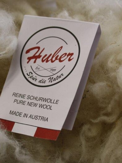 A label reading "Huber" is placed on a surface made of pure virgin wool. The label provides information about pure virgin wool, made in Austria. | © Huber Strick- und Walkwaren