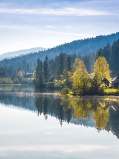 A quiet lake surrounded by trees and mountains. The colors of the trees are reflected in the water. | © TV Hochsteiermark/Fred Lindmoser