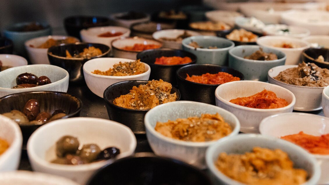 Eine Vielzahl von kleinen Schalen mit verschiedenen Dips und Oliven. Die bunten Schalen zeigen eine appetitliche Auswahl an Zutaten. | © Hummel Graz