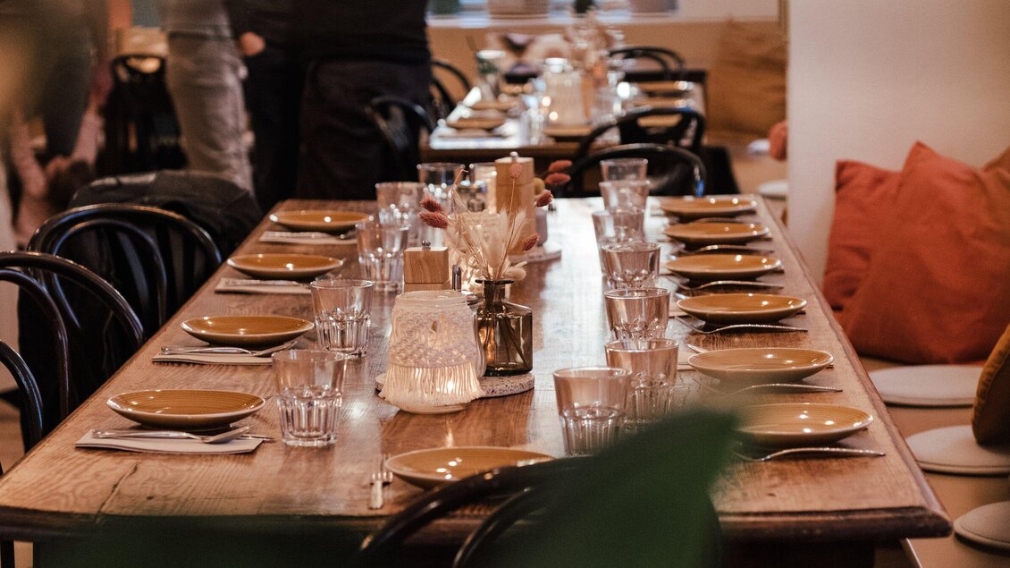 Ein langes Tischgedeck in einem Restaurant mit Tellern, Gläsern und dekorativen Elementen. Die Atmosphäre ist einladend und gemütlich. | © Hummel Graz