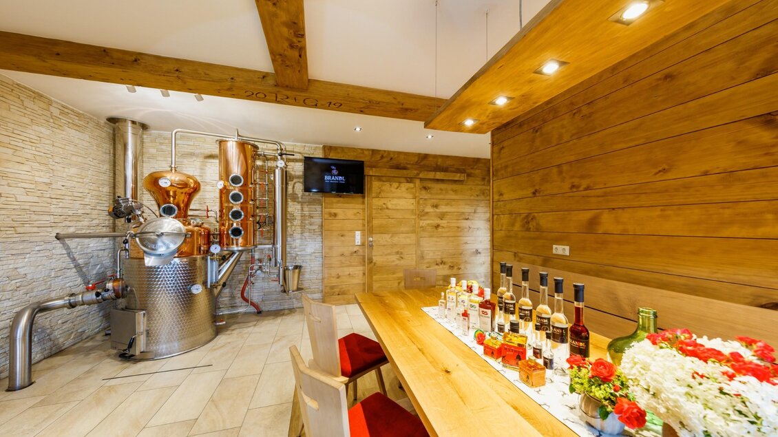 Ein gemütlicher Raum mit einer Holzdecke und einer großen Holztafel. Im Hintergrund steht eine Brennerei mit verschiedenen Flaschen auf dem Tisch. | © © Thomas Brandl Spirits