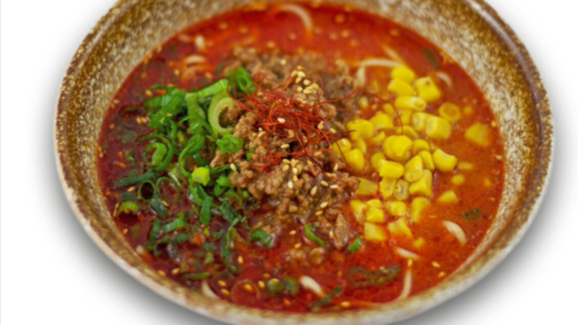 Eine Schüssel mit würziger Suppe, die Hackfleisch, Mais und Frühlingszwiebeln enthält. Die Brühe hat eine leuchtend rote Farbe und ist mit Gewürzen garniert. | © Ichi-Go Ichi-E