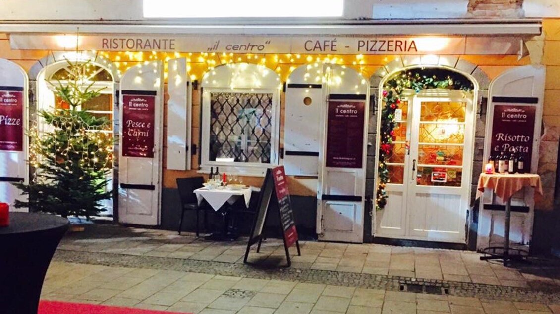 Ein einladendes Restaurant mit gemütlicher Beleuchtung und Weihnachtsdekoration. Draußen steht ein Tisch, und die Fenster sind festlich geschmückt. | © Il Centro
