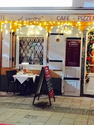 An inviting restaurant with cozy lighting and Christmas decorations. Outside, there is a table, and the windows are festively adorned. | © Il Centro