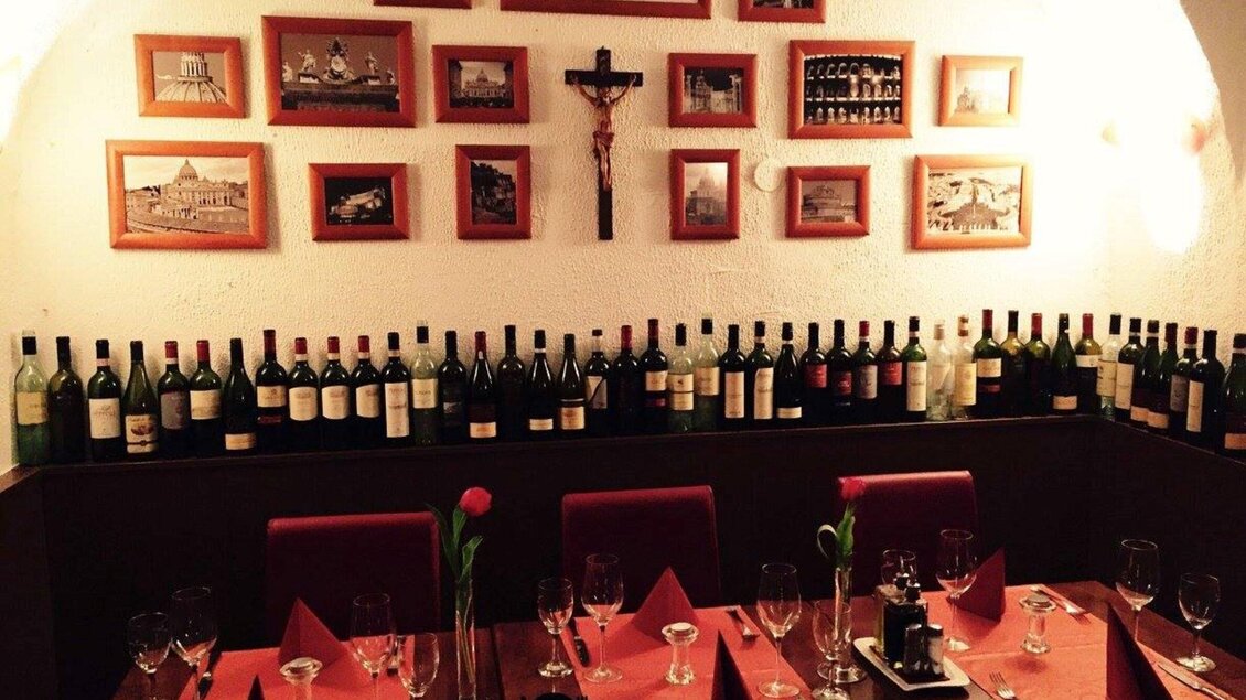 Ein gemütliches Restaurant mit Weinflaschen an der Wand. Es gibt rote Tischdecken und Gläser für die Gäste. | © Il Centro