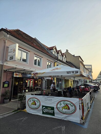 A cozy restaurant with an outdoor area on a city street. Tables are set under a large parasol, inviting guests. | © Il Gusto Classico