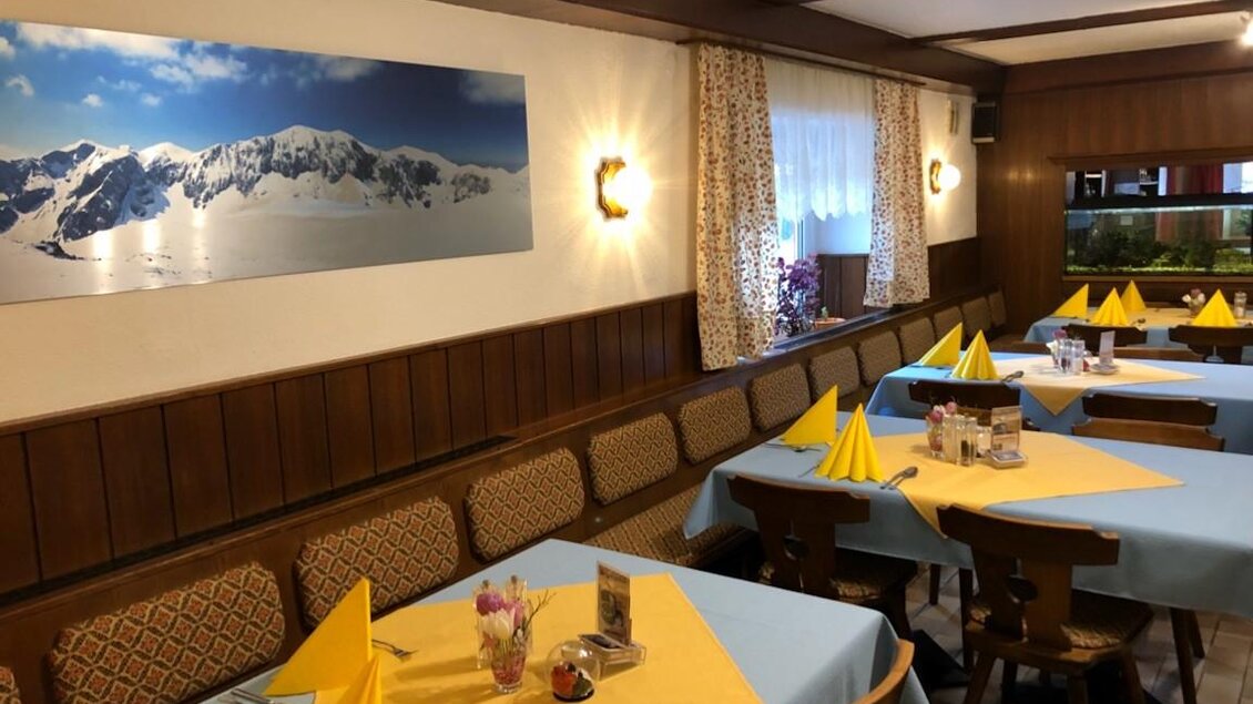 Ein gemütliches Restaurant mit Holzvertäfelung und hellen Tischen. Gelbe Servietten und eine beeindruckende Berglandschaft zieren die Wände.