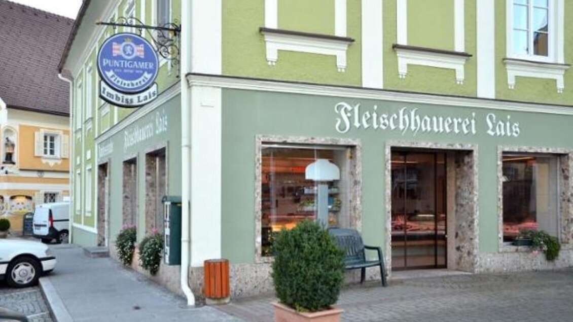 Ein Geschäft mit grünem Außenanstrich und großen Fenstern. Davor stehen Pflanzen und eine gemütliche Sitzgelegenheit. | © Imbisstube Lais Werner