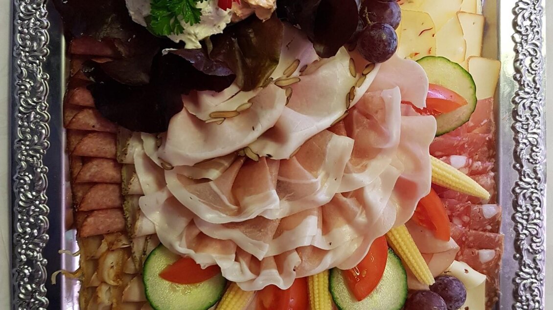 Eine appetitliche Platte mit verschiedenen Wurst- und Käsesorten, dekoriert mit Gemüse und Trauben. Die Anordnung ist bunt und ansprechend. | © Imbisstube Lais Werner