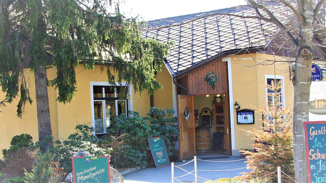 Ein gemütliches Restaurant mit gelber Fassade und einem einladenden Eingang. Umgeben von Bäumen und grünen Pflanzen. | © In's Pfandl