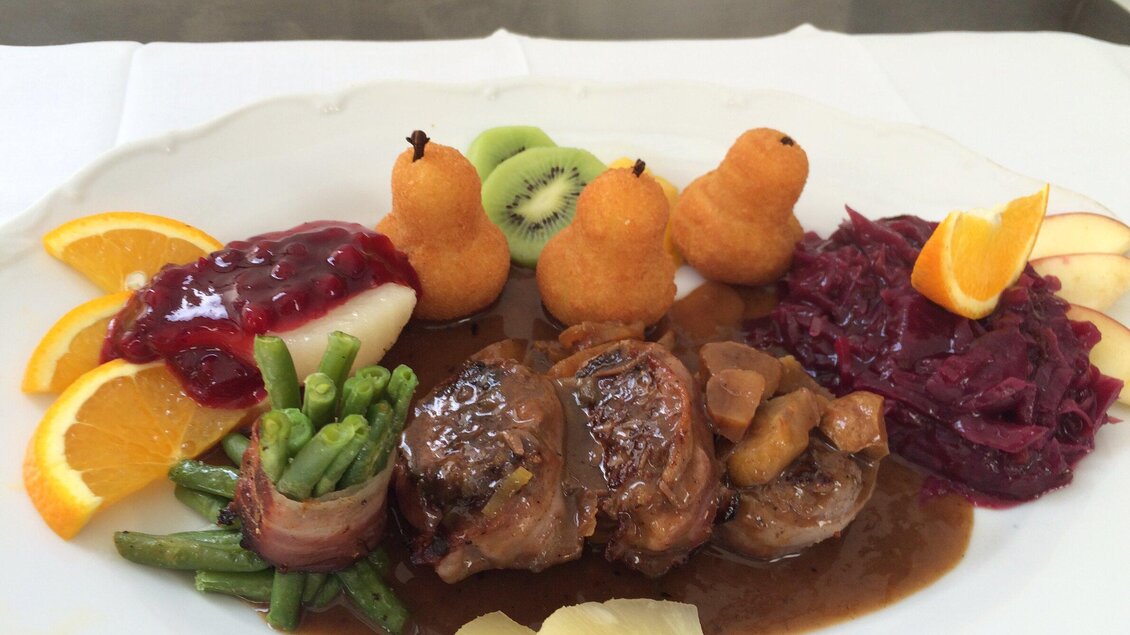 Ein schön angerichteter Teller mit Fleisch, grünen Bohnen, Rotkohl und einer fruchtigen Beilage. Dekoriert mit Obst und Soße. | © In's Pfandl