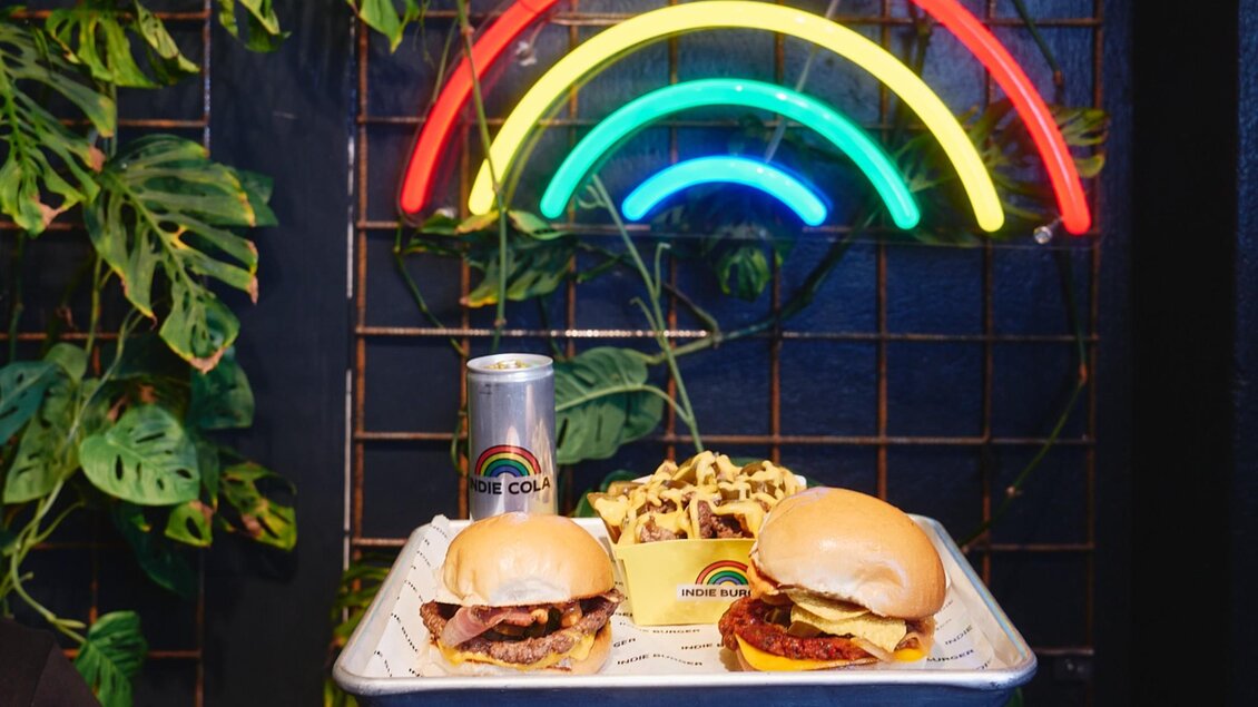 Serviertablett mit zwei Burgern, Fries mit Sauce und Indie Cola vor Neonwand. | © Indie Burger - Samuel Kuro