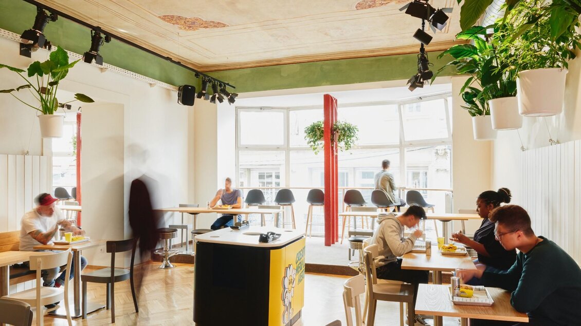 Heller Gastraum mit historischen Deckenmalereien, Pflanzen und Gästen. | © Indie Burger - Samuel Kuro