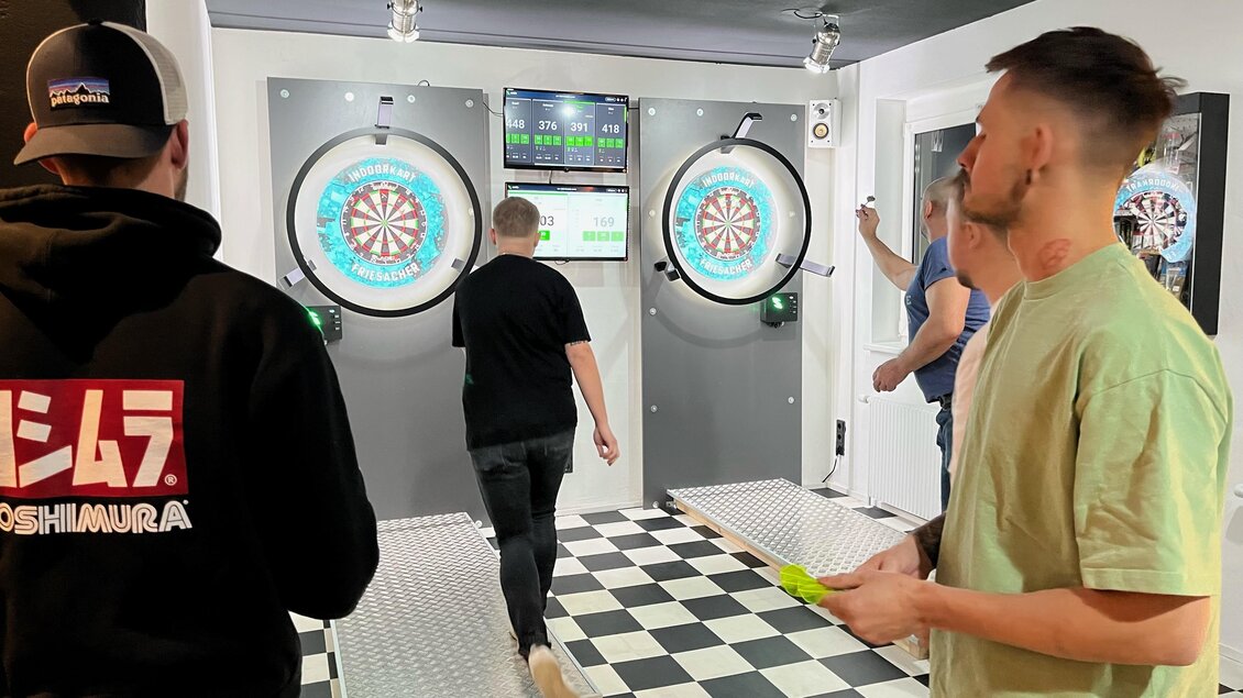 Eine Gruppe von Menschen spielt Darts in einem modernen Spielraum. Die Wände sind mit Dartscheiben und Bildschirmen ausgestattet. | © Indoorkart Spielberg