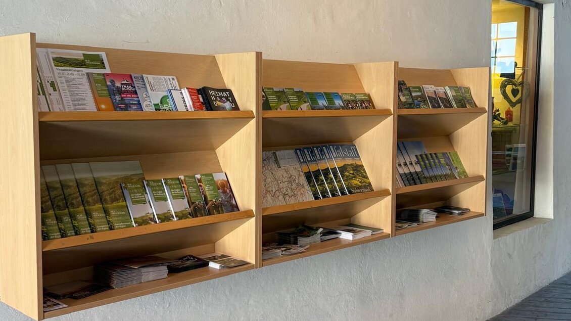 Eine Holzregalwand mit Informationsmaterialien und Broschüren. Die Wand befindet sich in einem hellen Innenraum. | © TVB Südsteiermark