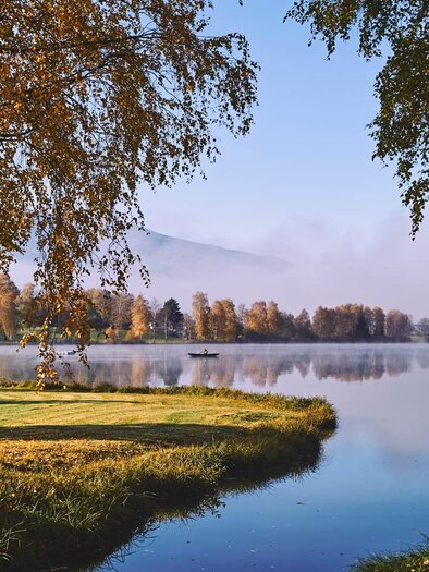 Ein ruhiger See umgeben von bunten Herbstbäumen. Der Himmel ist klar, und der Nebel liegt sanft über dem Wasser. | © Infobüro Irdning