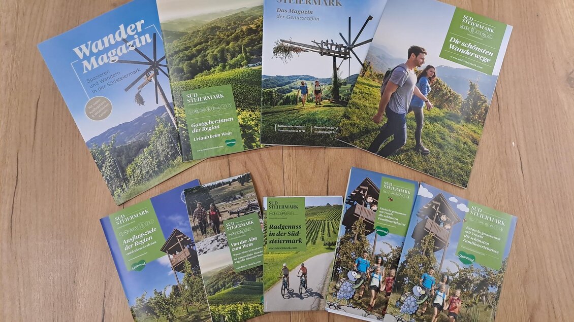 Eine Sammlung von Wanderbroschüren liegt auf einem Holzfußboden. Die Magazine zeigen Bilder von Naturwegen und Aktivitäten im Freien. | © Tourismusverband Südsteiermark