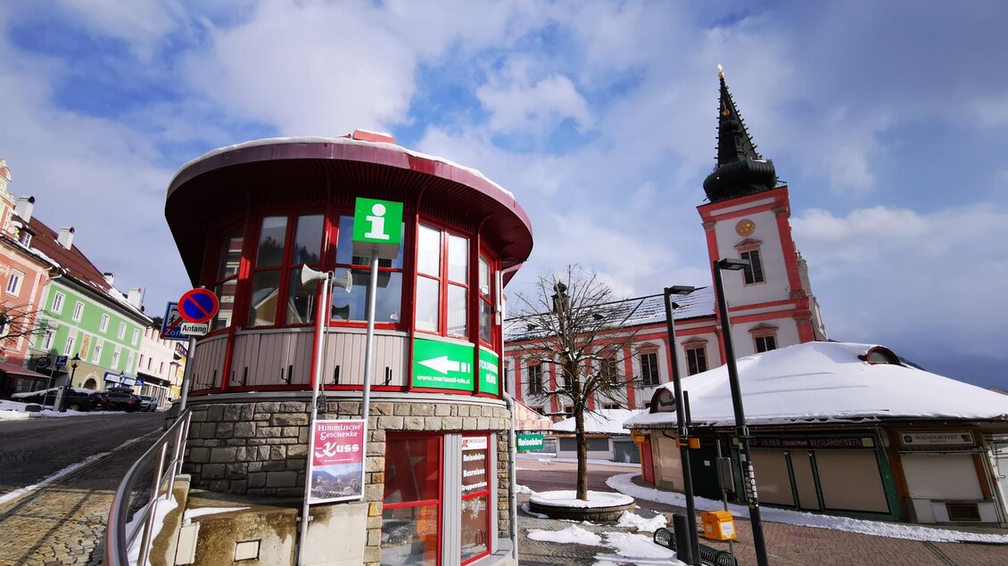 Ein Informationsstand in einer verschneiten Stadt. Im Hintergrund sieht man eine Kirche mit einem hohen Turm. | © TV Hochsteiermark