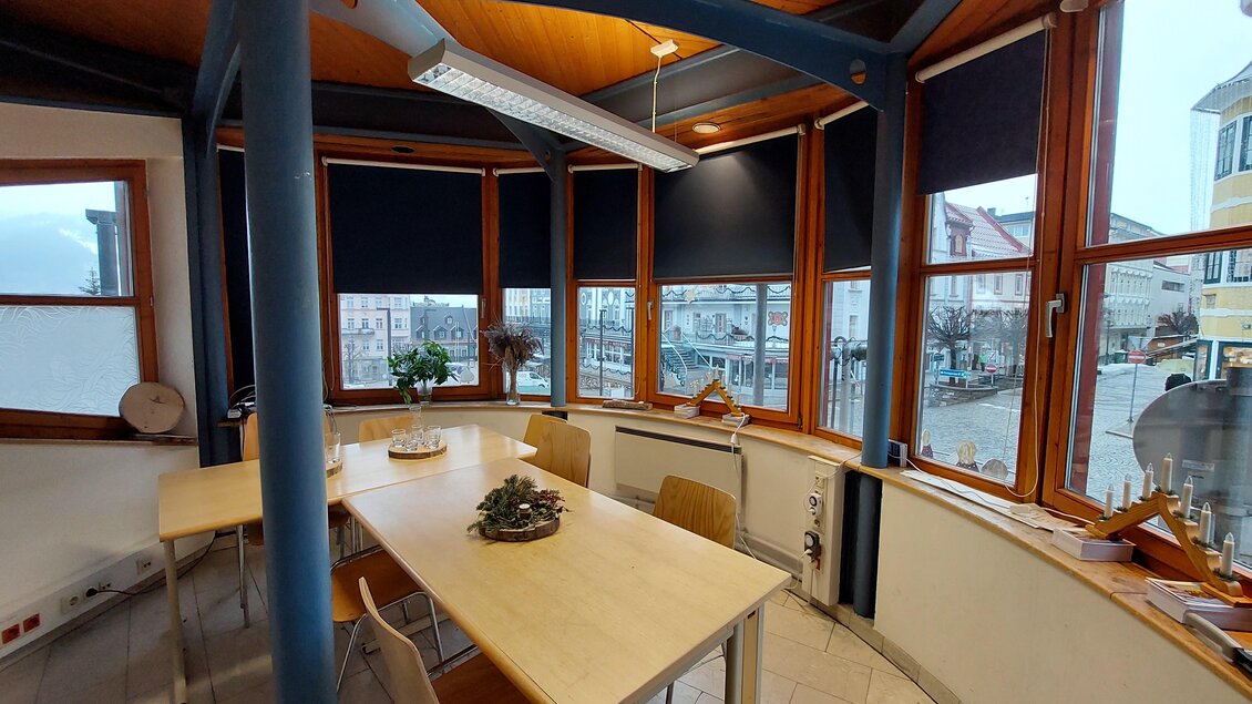 Ein heller Raum mit großen Fenstern und einem Tisch in der Mitte. Draußen ist eine malerische Stadtansicht zu sehen. | © TV Hochsteiermark