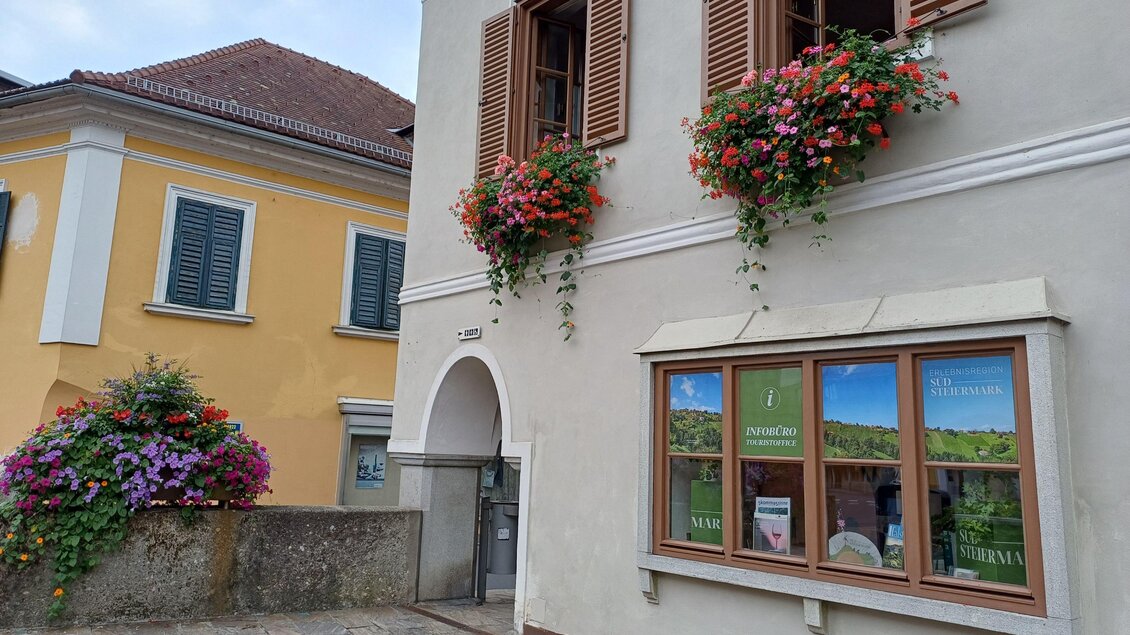 Ein charmantes Gebäude mit bunten Blumenkästen und Holztüren. Die umliegenden Häuser haben fröhliche Farben und verleihen der Straße eine einladende Atmosphäre. | © TVB Südsteiermark - Irene Löschnig