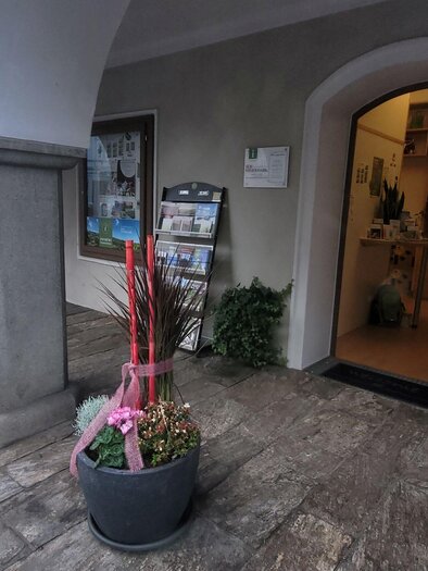 Ein Eingangsbereich mit Säulen und einer offenen Tür. Vor der Tür stehen große Pflanzen mit roten Dekorationen. | © TV Südsteiermark - Irene Löschnig