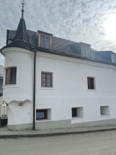 Ein elegantes, weißes Gebäude mit einem spitzen Turm. Die Fassade ist schlicht und modern, umgeben von einer ruhigen Straße. | © Greitner Michaela