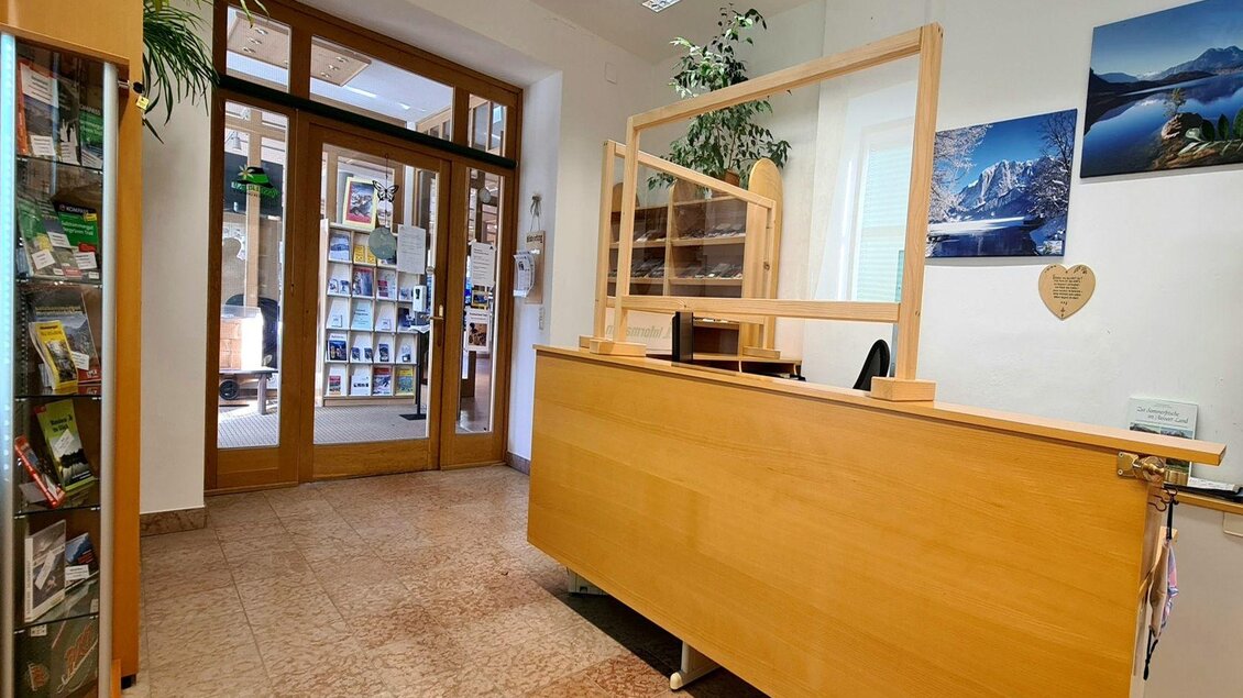 Ein Empfangsbereich mit einem Holzschalter und großen Fenstern. An der Wand sind Bilder und Pflanzen zu sehen, die eine freundliche Atmosphäre schaffen. | © Stephanie Bor