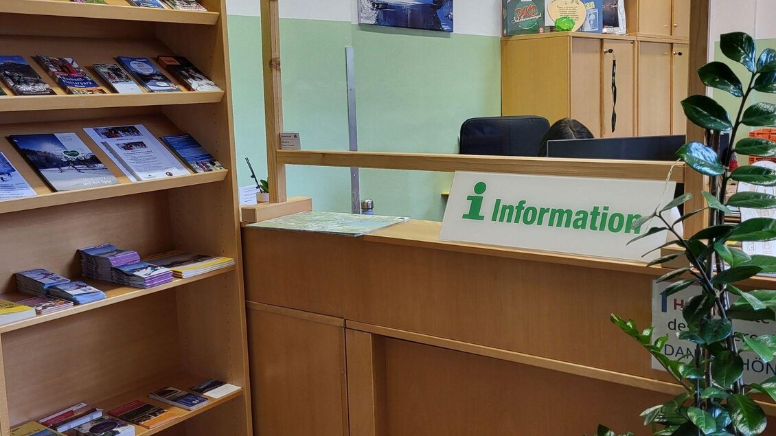 Ein Informationsschalter mit einem grünen "Information"-Schild. Im Hintergrund sind Regale mit verschiedenen Informationsmaterialien und eine Pflanze zu sehen. | © Petra Kirchschlager