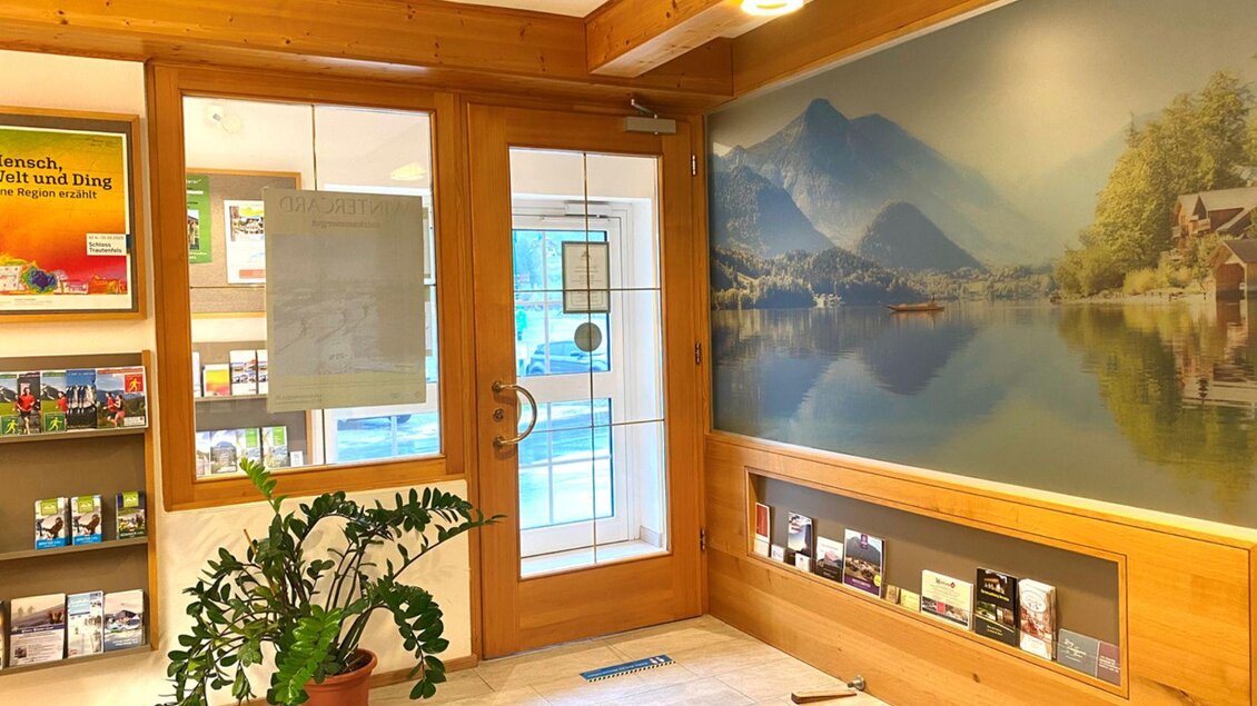 Ein einladender Empfangsbereich mit Holzverkleidung und einer großen Fensterfront. An der Wand ist ein Malerei eines ruhigen Sees mit Bergen im Hintergrund zu sehen. | © Bettina Scheck