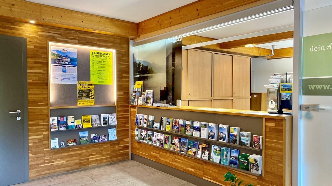 Ein moderner Empfangsbereich mit Holzverkleidung und einem einladenden Informationsschalter. An der Wand hängen zahlreiche Broschüren und Informationen. | © Bettina Scheck
