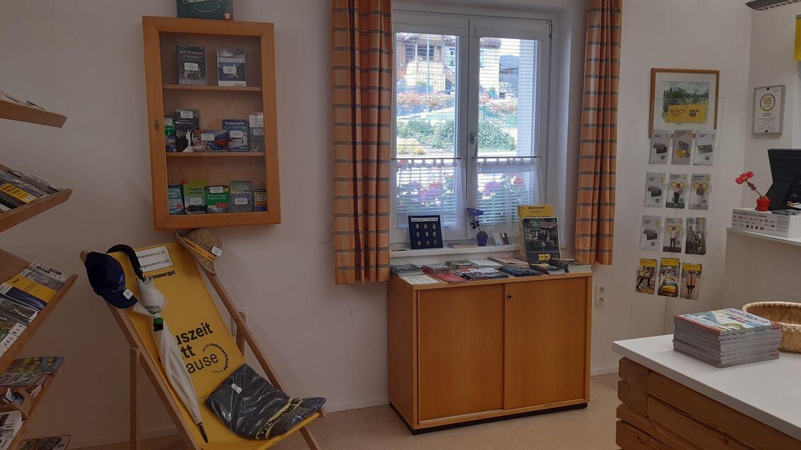 Ein einladender Raum mit Holzregalen, gefüllt mit Informationsmaterialien. Am Fenster ist ein gemütlicher Sessel mit Blick nach draußen. | © TVB Ausseerland Salzkammergut/Raunigg