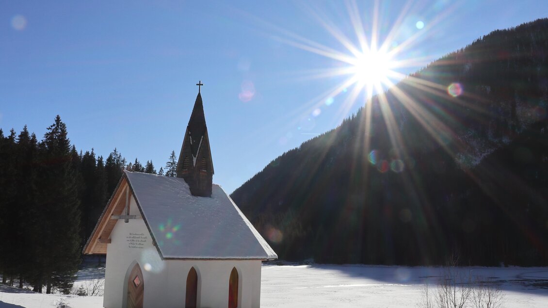 Eine kleine Kirche steht in einer verschneiten Landschaft. Die Sonne scheint hell über die Berge und das Eis. | © WEGES