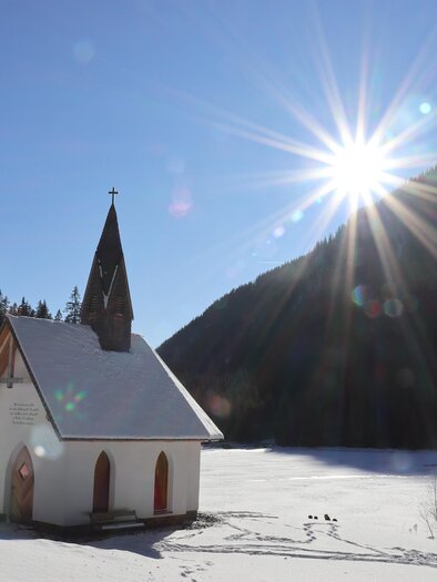 A small church stands in a snowy landscape. The sun shines brightly over the mountains and the ice. | © WEGES