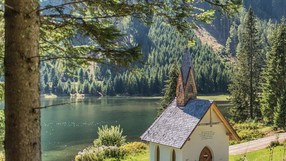 Eine kleine Kirche steht malerisch am Ufer eines ruhigen Sees, umgeben von hohen Bäumen und Bergen. Der Ort strahlt eine friedliche und idyllische Atmosphäre aus. | © Anita Fössl