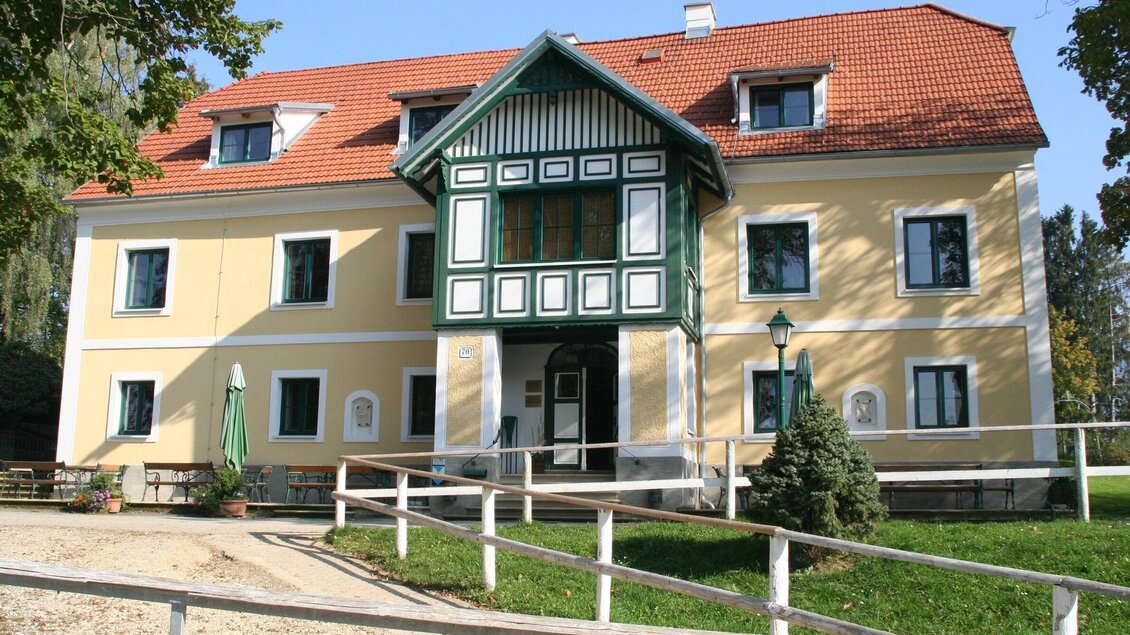Ein historisches Gebäude mit gelber Fassade und grünen Akzenten. Vor dem Haus stehen Bäume und eine Geländerfarm. | © Piet Hoyos
