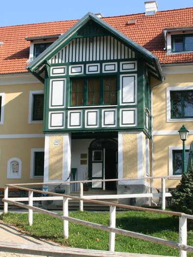 Ein historisches Gebäude mit gelber Fassade und grünen Akzenten. Vor dem Haus stehen Bäume und eine Geländerfarm. | © Piet Hoyos