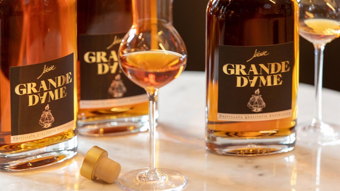 Eine elegante Präsentation von Grande Dôme-Flaschen auf einem Tisch. Im Vordergrund steht ein Glas mit hochwertigem Getränk. | © Brennerei Jöbstl