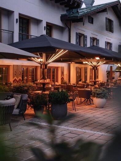 A cozy terrace with modern furniture and sun umbrellas. The surroundings are quiet and inviting, perfect for a relaxed evening. | © JOHANN Schladming