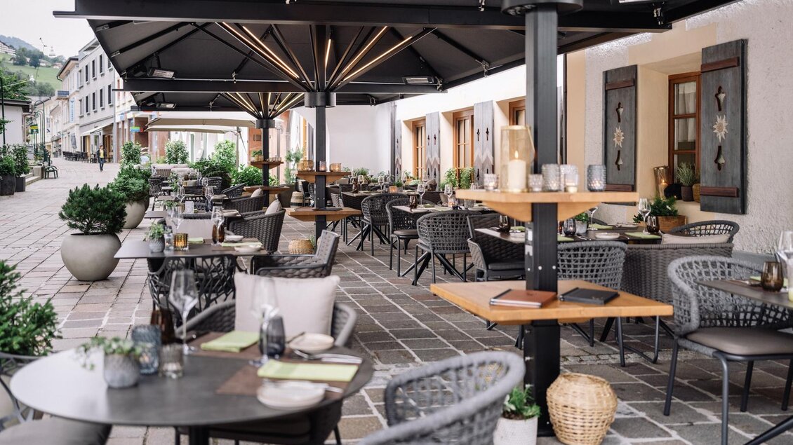 Ein gemütlicher Außenbereich eines Restaurants mit modernen Tischen und Stühlen. Die Umgebung ist grün und einladend, ideal für ein Essen im Freien. | © JOHANN Schladming